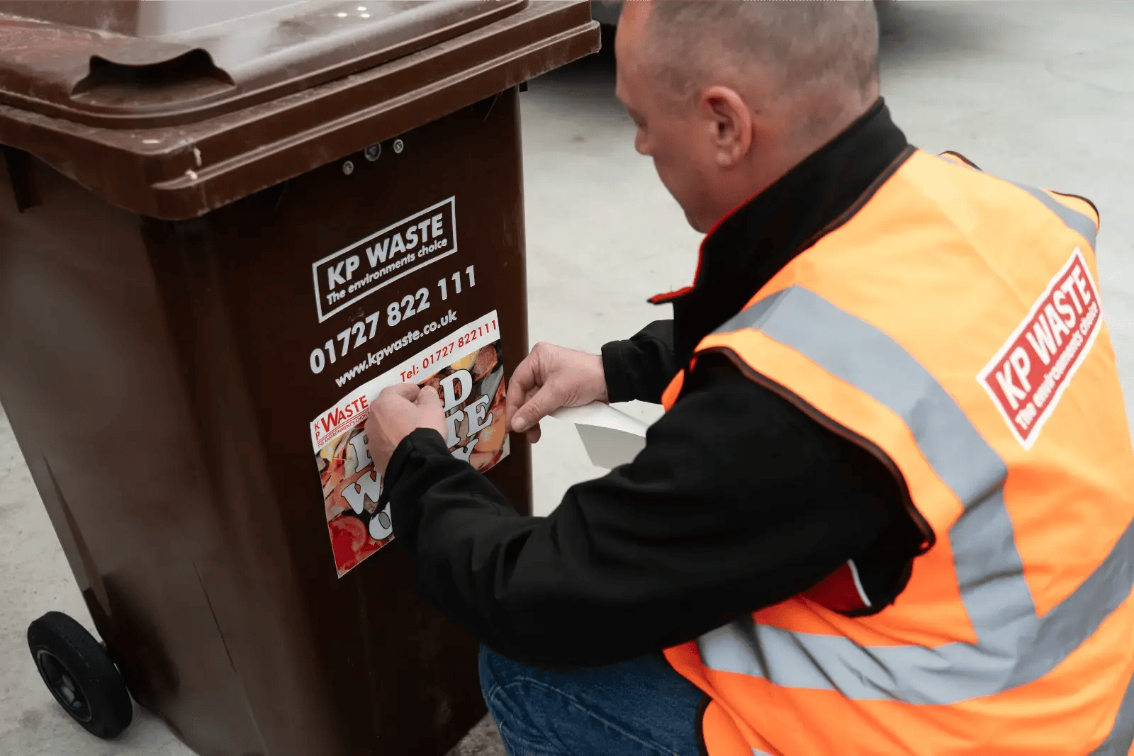 KP Waste staff member applying food waste recycling information to a commercial wheelie bin. KP Waste staff member applying food waste recycling information to a commercial wheelie bin.
