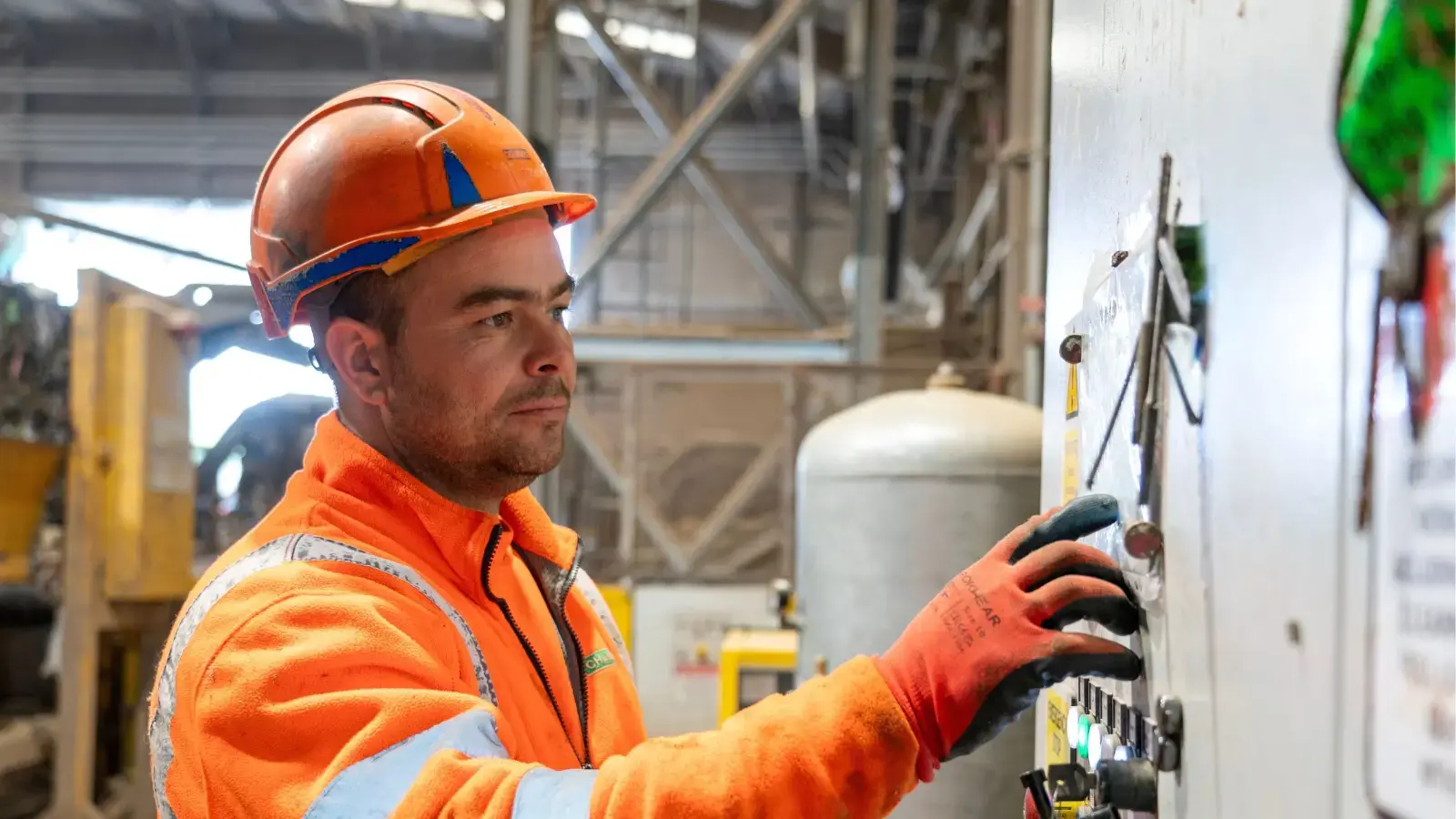 Chambers Waste Management operative in orange PPE and hard hat operating controls on industrial machinery inside a recycling facility